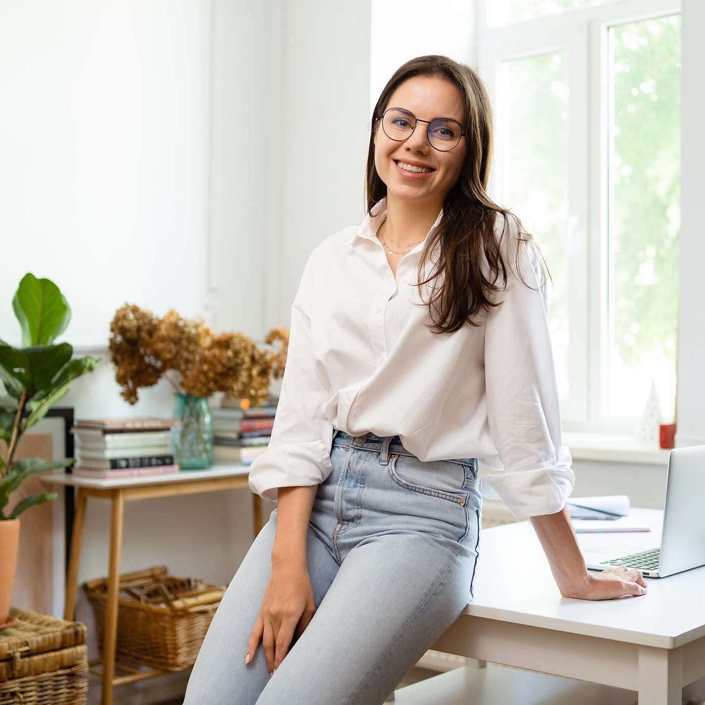 Image of young cheery positive beautiful business woman sitting indoors in office or home office using laptop computer.